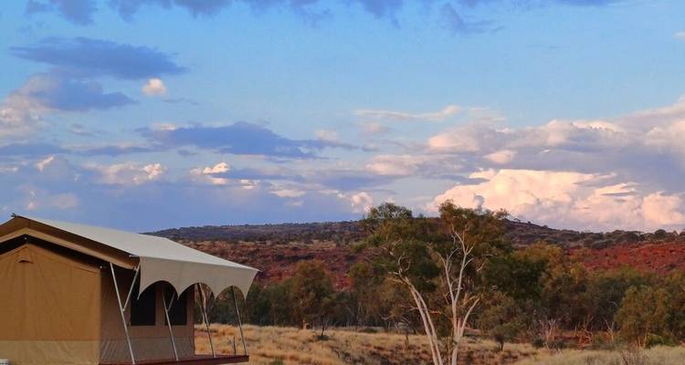Une tente dans l'arrière-pays avec des arbres et des collines en arrière-plan.
