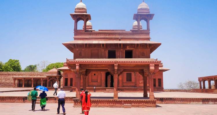 An ancient red brick building with people walking and umbrellas.