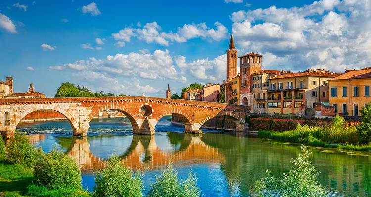 Pont de pierre historique et clocher au bord d'une rivière sous un ciel bleu.