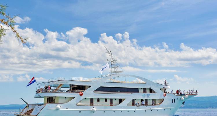 Luxurious yacht sailing in clear waters with mountains in the distance.
