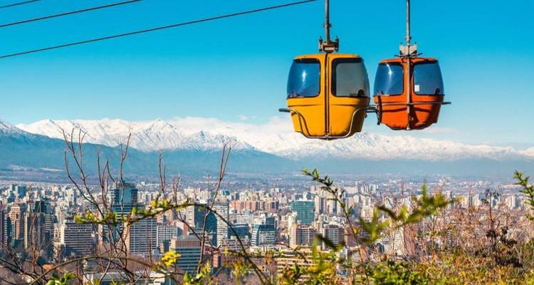 Deux téléphériques colorés suspendus au-dessus de la ville de Santiago avec la chaîne des Andes en arrière-plan.