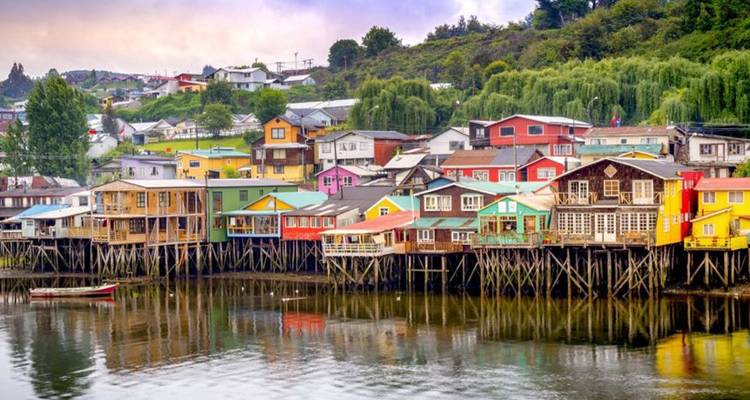 Rangée de maisons sur pilotis en bois peint de couleurs vives se reflétant dans une eau calme sur l'île de Chiloé.