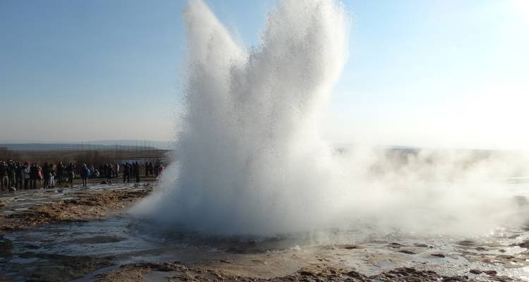 Een geiser die uitbarst met een dramatische waterkolom en stoom omringd door toeschouwers.