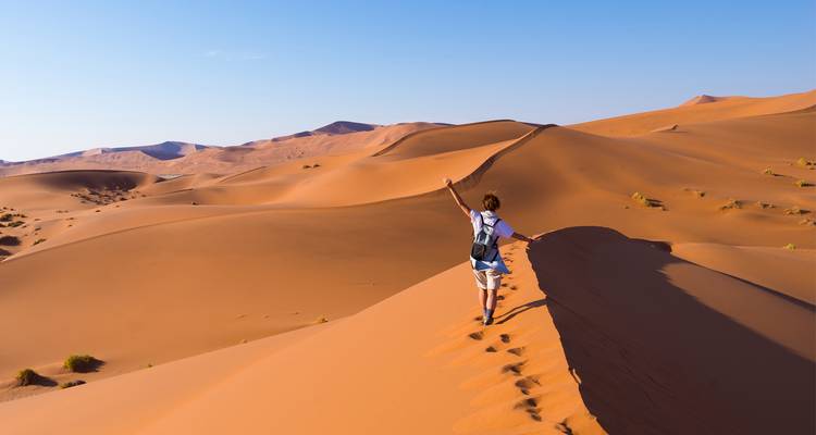 Persona caminando por grandes dunas de arena en un paisaje desértico.