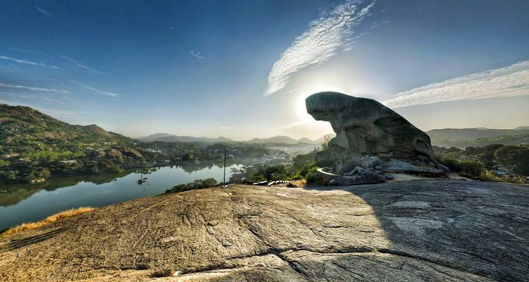 Rotsformatie bij een rivier met een bergachtig landschap op de achtergrond.