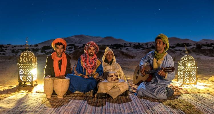 Desert camp with people in traditional attire during nighttime