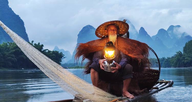 Fisherman on a boat holding a lantern on a river.