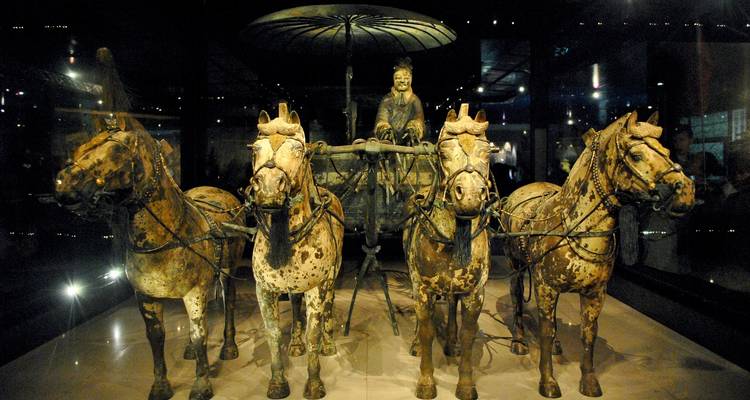 Terracotta army horses and chariot under dim lighting.