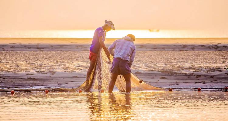 Pêcheurs tirant des filets au coucher du soleil près de l'eau.