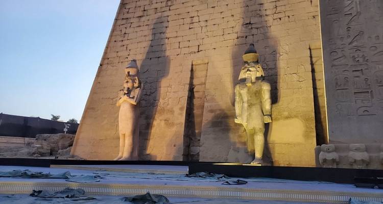Zwei beleuchtete Statuen vor einer großen antiken Mauer in der Dämmerung.