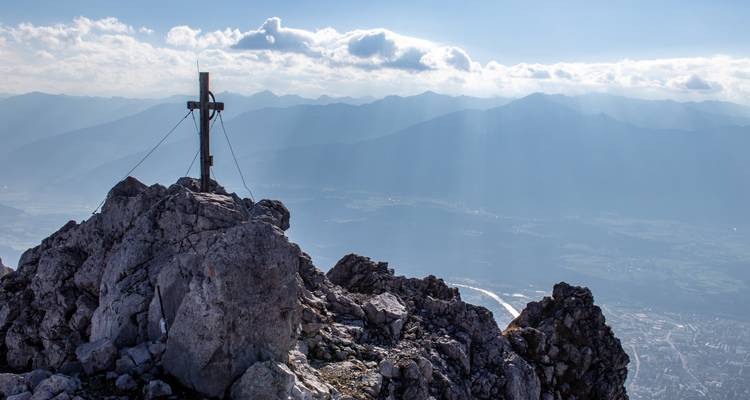 Rotsachtige bergpiek met kruis, uitkijkend over een uitgestrekt landschap.