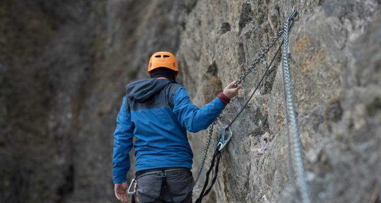 Klimmer met een oranje helm die zich vastmaakt aan een rotswand.