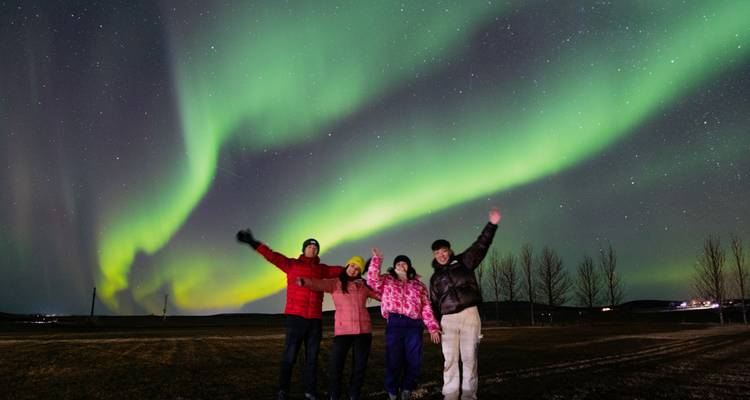 Groupe posant sous des aurores boréales vert vif dans un ciel nocturne dégagé.