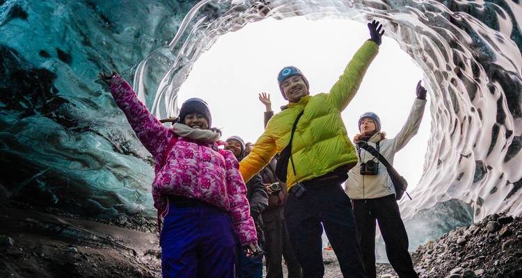 Un groupe applaudit à l'intérieur de l'entrée circulaire d'une grotte de glace glaciaire.