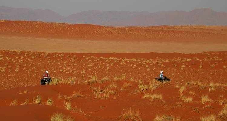 Deux personnes conduisant des quads sur des dunes de sable rouge.