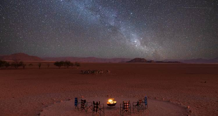 Ciel nocturne étoilé avec un feu de camp et des chaises disposées en cercle.