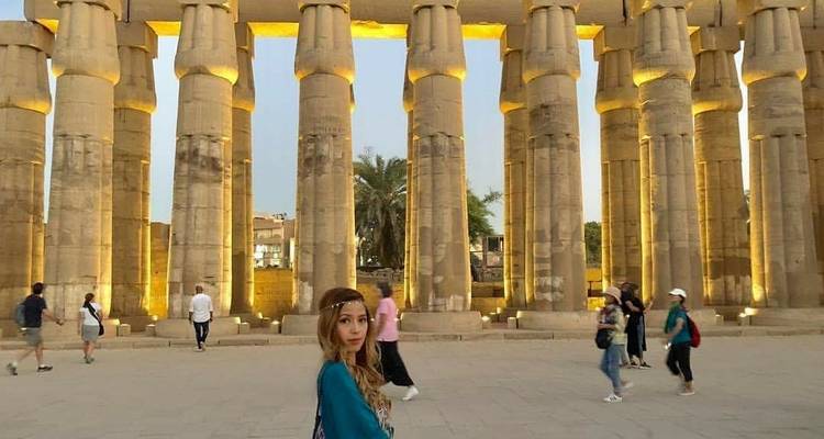 Touristen wandeln zwischen beleuchteten antiken Säulen in der Dämmerung.
