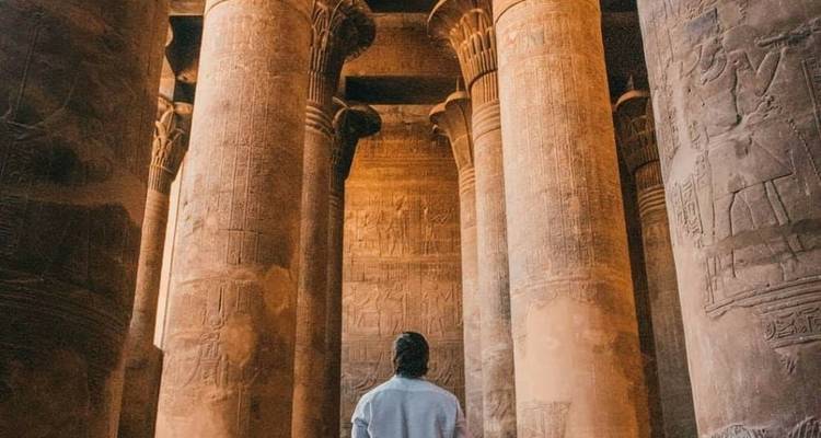 Person, die zwischen großen antiken Säulen mit Hieroglyphen steht.