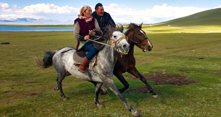 Two people riding horses across a grassy landscape.