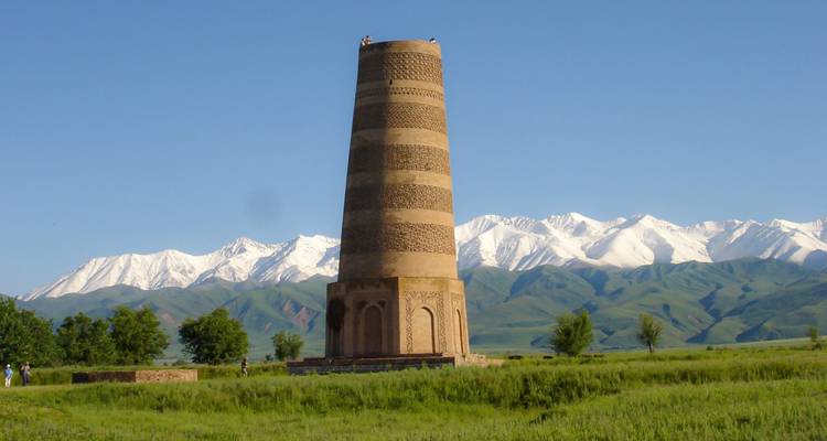 A tall ancient tower with snowy mountains behind it.