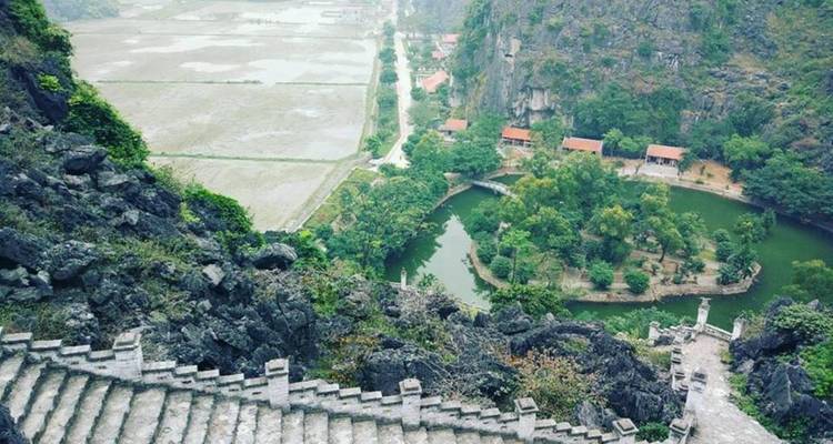 Staircase leading down a rocky cliff with lush greenery and a small body of water in the valley.