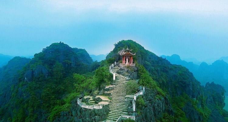 A stunning view of a temple at the peak of a mountain surrounded by foggy hills.