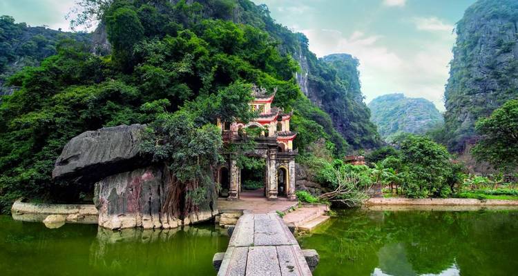 A beautiful temple gate among lush greenery with towering cliffs behind.