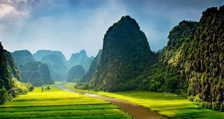 A scenic view over a winding river through lush green fields with limestone mountains.