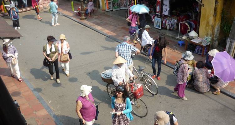 Drukke straatscène met mensen die lopen en fietsen, kramen vol met goederen.