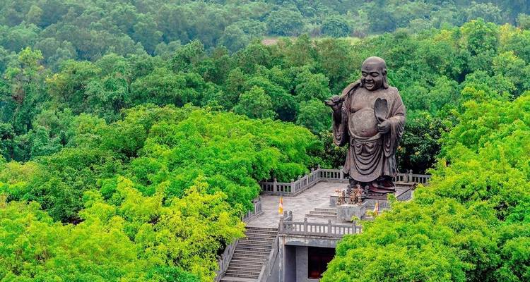 Groot standbeeld van een Lachende Boeddha omringd door weelderig groen.