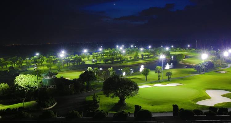 Gut beleuchteter Golfplatz bei Nacht mit Wasserspielen und Bäumen