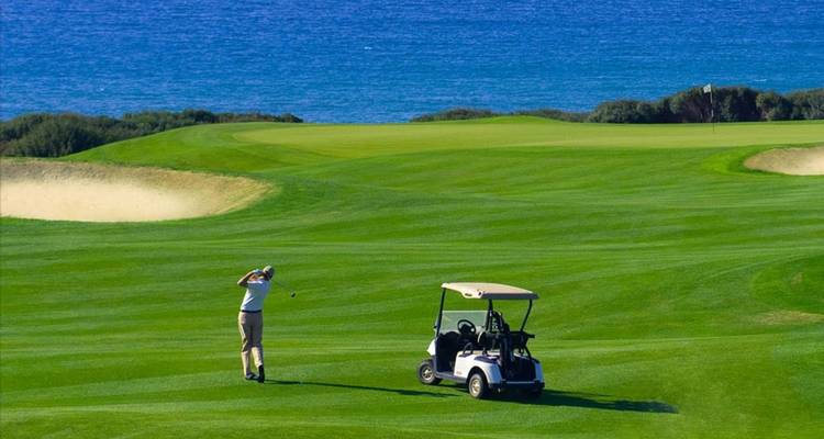 Golfer auf einem Golfplatz mit Meerblick und einem Golfcart in der Nähe.