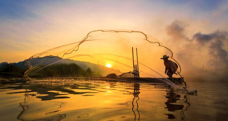 Fischer wirft ein Netz bei Sonnenuntergang über dem Wasser.