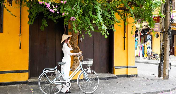 Vrouw in traditionele kledij met fiets onder bloeiende boom.
