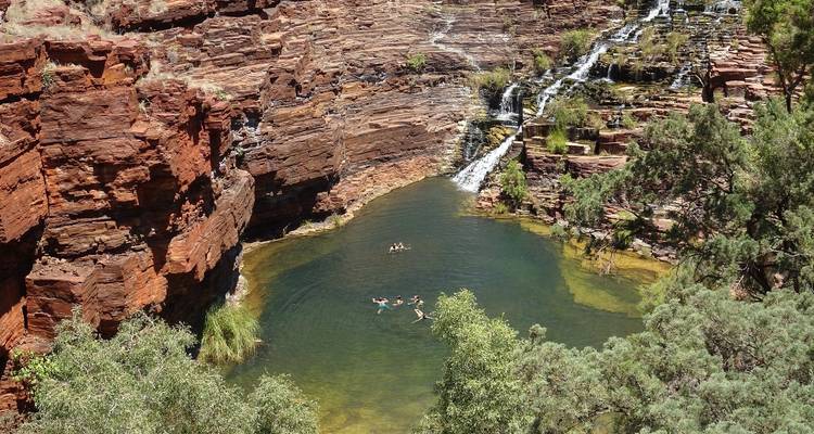 Wasserfall in einer zerklüfteten Schlucht mit Schwimmern, die das Wasser genießen, wahrscheinlich im Karijini-Nationalpark.