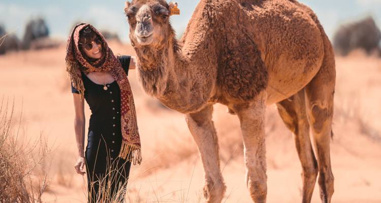 Vrouw die poseert met een kameel op een zandig landschap.
