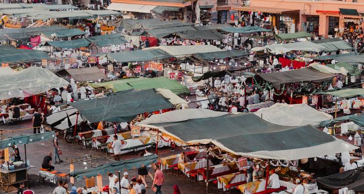 Une vue aérienne dense d'un marché en plein air animé rempli d'auvents verts, de marchandises et de foules d'acheteurs.