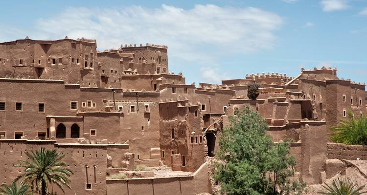 Des bâtiments de kasbah fortifiés de couleur terre s'élèvent contre un ciel bleu, mettant en valeur l'architecture marocaine classique.