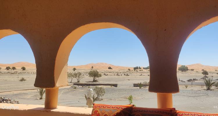 Paysage désertique encadré par des arches triples d'un bâtiment en adobe ; filigrane de smartphone présent.