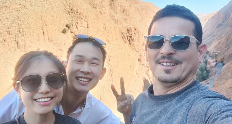 Trois amis souriants prennent un selfie sur fond d'une gorge rocheuse escarpée en plein jour.