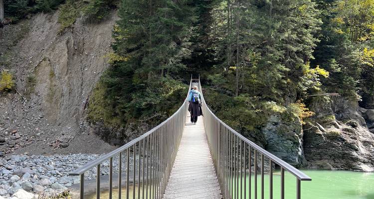 Persona caminando por un puente colgante sobre un río.