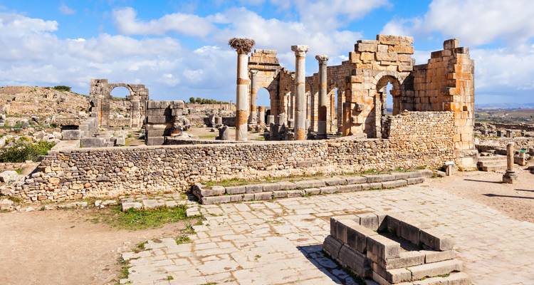 Ruinas romanas antiguas con arcos y columnas bajo un cielo azul.