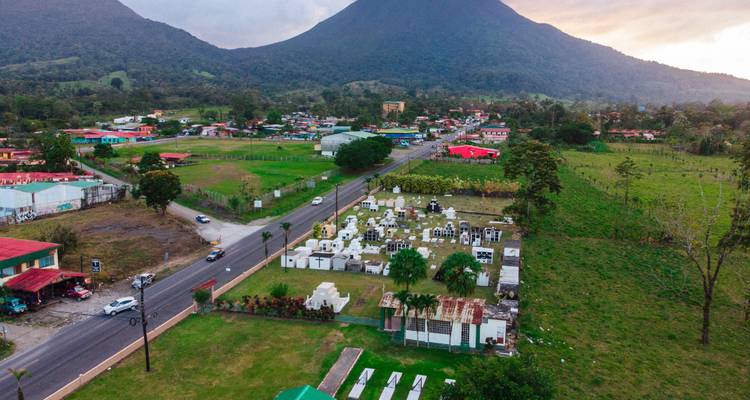 Dorf und Friedhof nahe Straßen mit Bergen im Hintergrund.