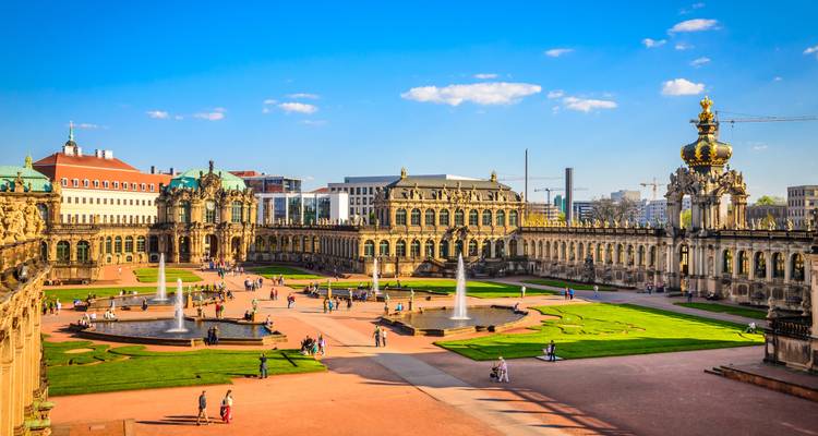 Les visiteurs se promènent dans les grandes cours baroques et les fontaines du palais Zwinger de Dresde sous un ciel bleu éclatant.