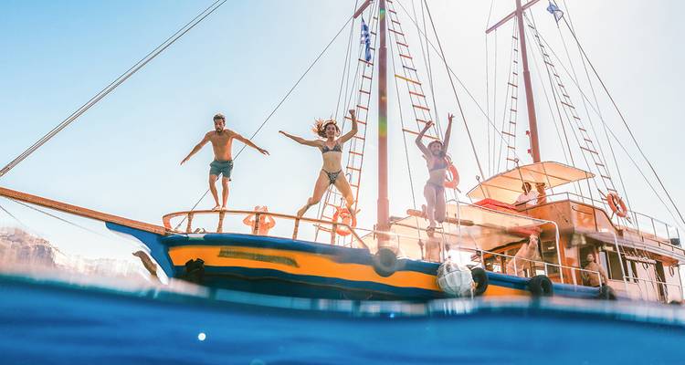 Des voyageurs sautent d'un voilier en bois coloré dans les eaux claires de la mer Égée sous un soleil éclatant.