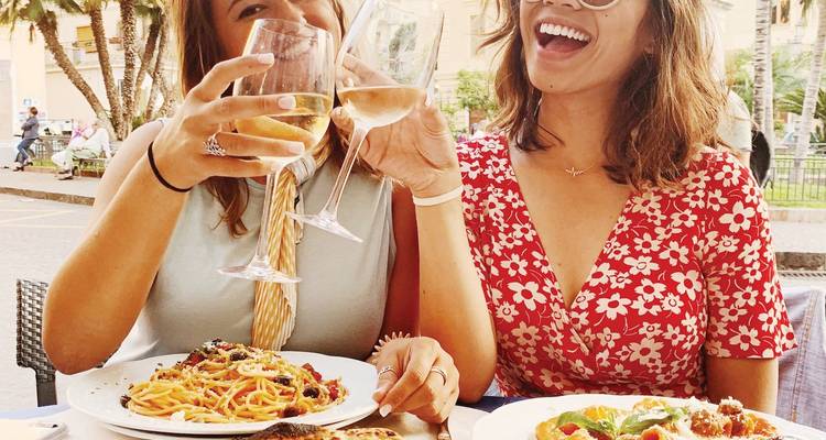 Twee vrienden proosten met witte wijn boven borden verse pasta en pizza bij een Italiaans café in de buitenlucht.