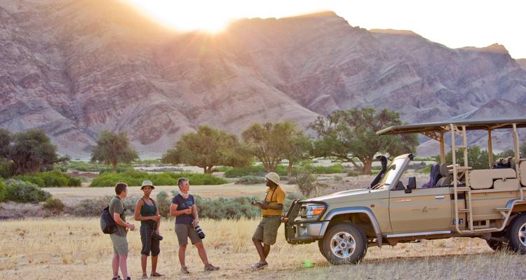 Safari-Gruppe mit einem Führer und Fahrzeug in einer Wüstenumgebung.