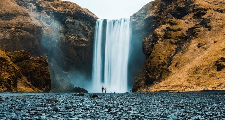 Skogafoss waterfall with two people standing at its base.