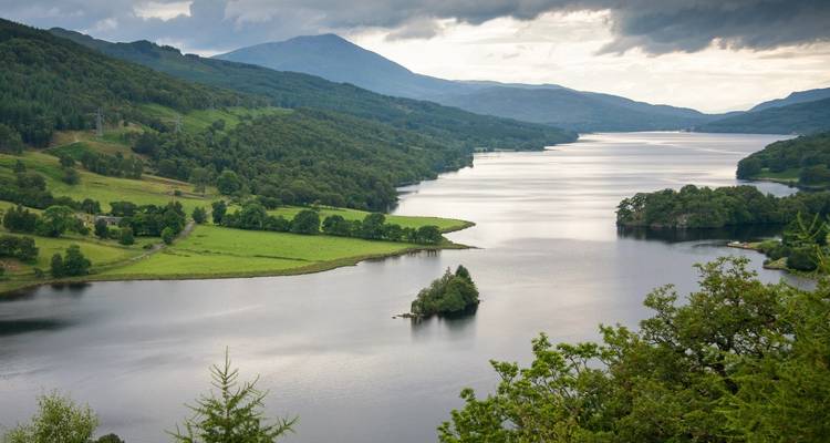 Sereno lago de agua dulce serpenteando entre colinas verdes escocesas bajo un cielo nublado