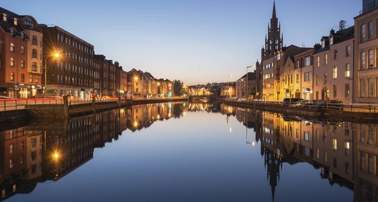 Avondstadsgezicht met historische gebouwen perfect weerspiegeld in een kalme rivier onder een heldere schemerende hemel.
